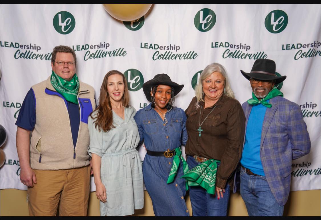 A group of people in western clothes standing in front of a Leadership Collierville Banner